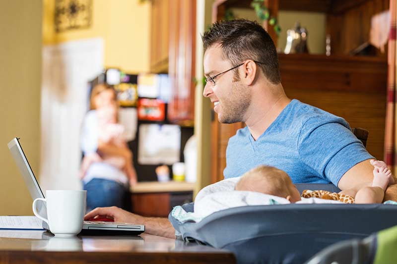 Man working on laptop with a baby on the desk